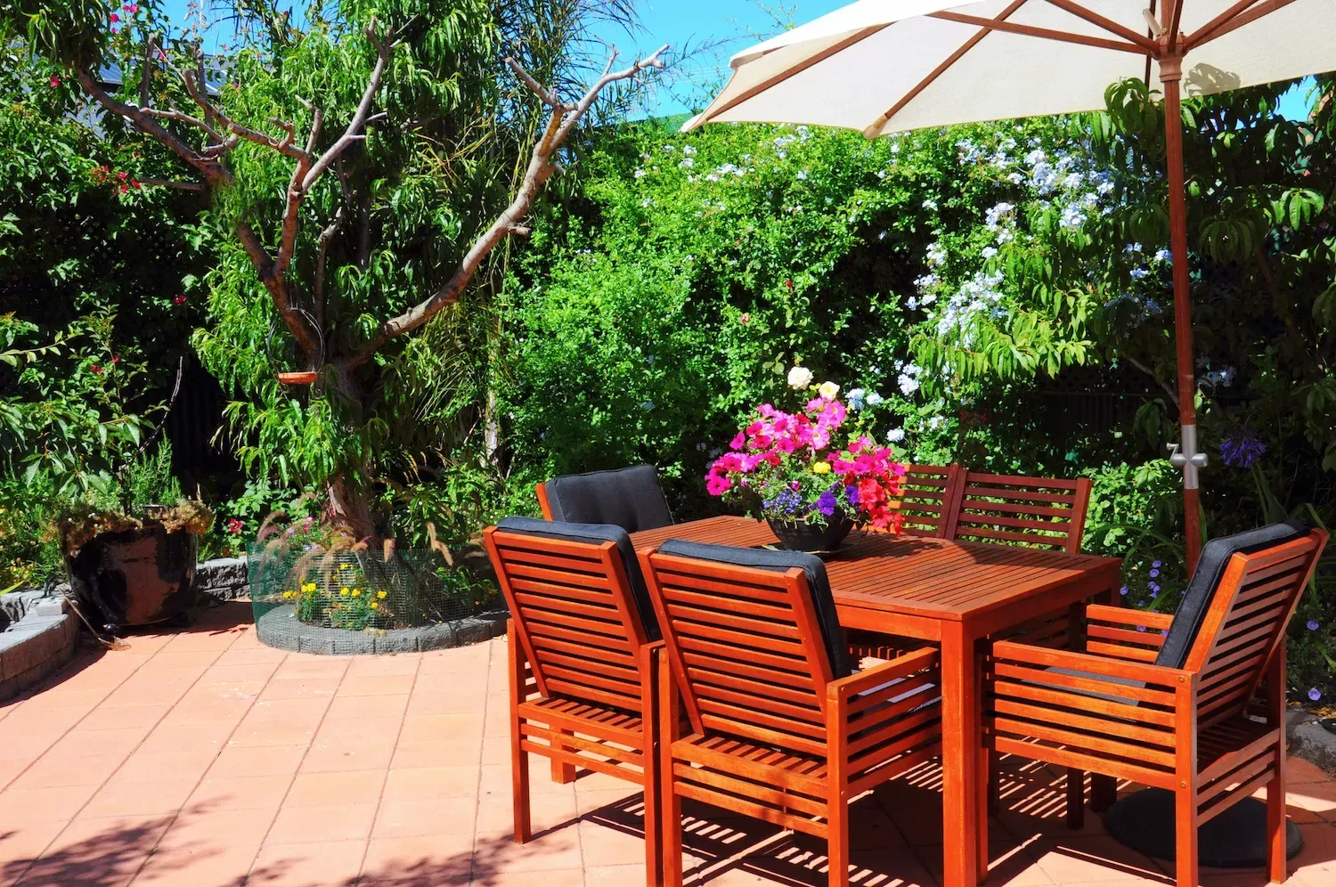 Outdoor timber dining table and chairs set up on a paved patio surrounded by garden
