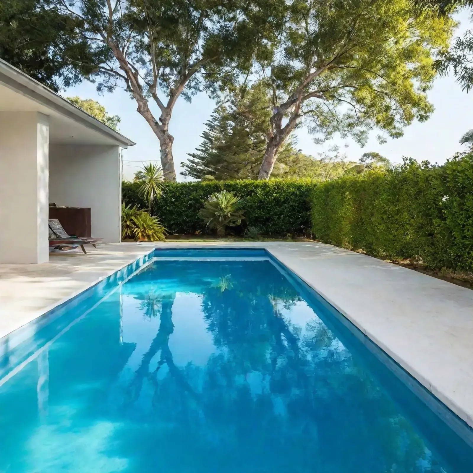 Long lap pool bordered by paving and lawn beneath established trees