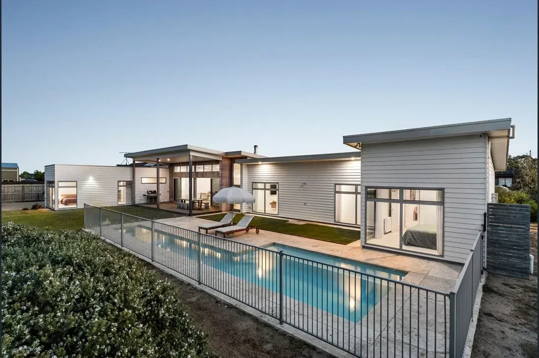 Modern home with an in-ground pool, glass fencing and travertine paving at dusk