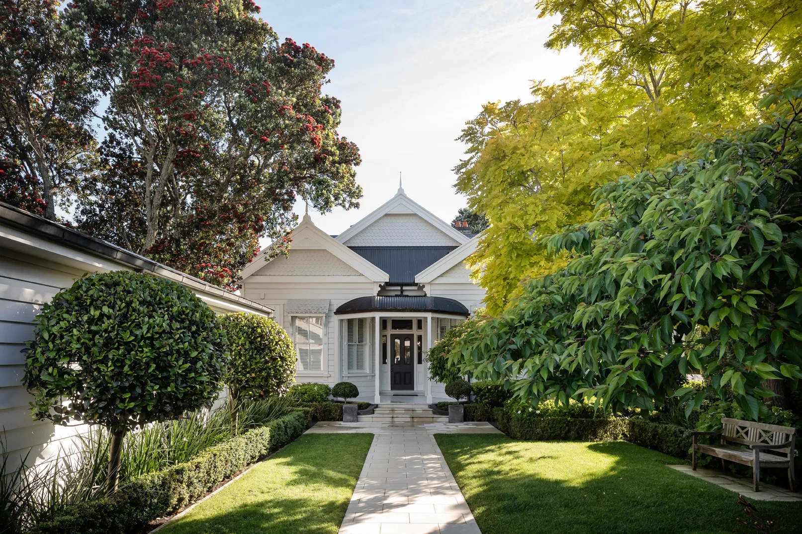 Classic white weatherboard home with manicured hedges and garden beds